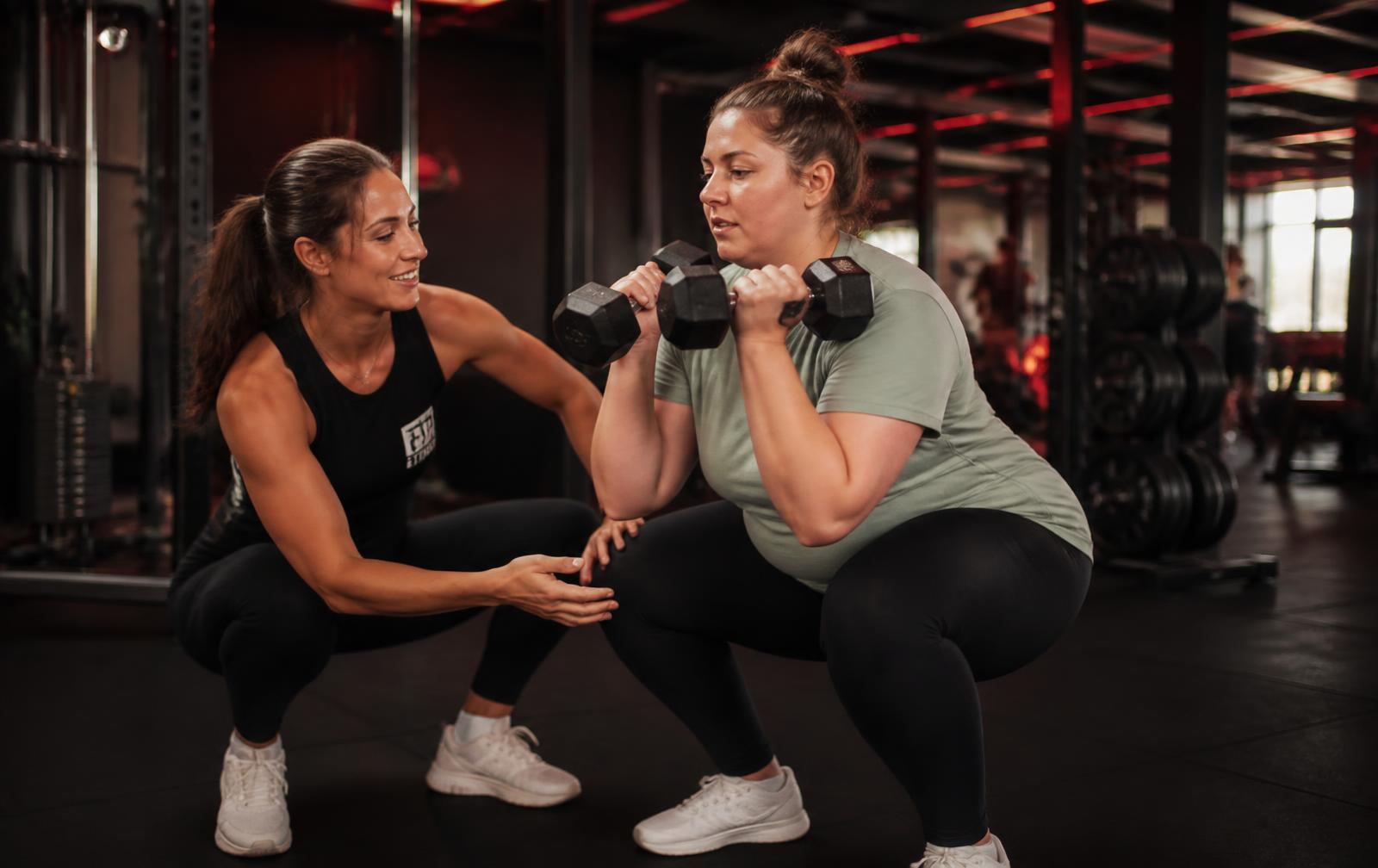 A Burn Fitness coach teaching a new member proper squat form